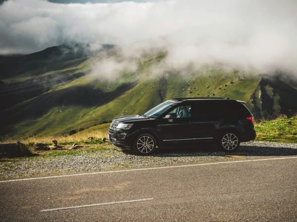 Un SUV negro estacionado al borde de una carretera en un paisaje montañoso, con nubes bajas cubriendo las colinas verdes.