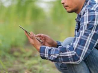 Agricultor utilizando uma tablet no campo, ilustrando a digitalização do setor agrícola.