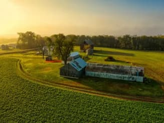 Imagen aérea de finca rústica con vivienda, invernadero y cultivos agrícolas.