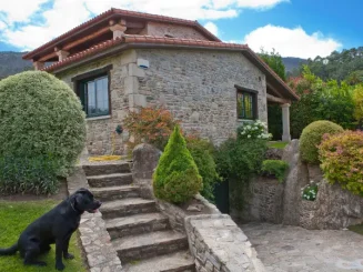 Casa rural de piedra con un perro en el jardín.