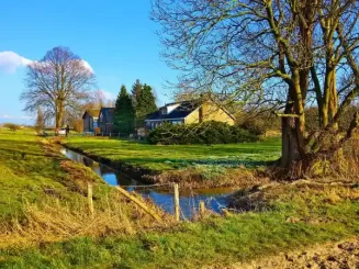 Paisaje rural con casas y terreno junto a un arroyo.
