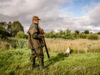 Cazador con escopeta y perro en el campo durante una jornada de caza.
