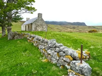 Casa antiga numa propriedade rústica rodeada por campo verde e muro de pedra.